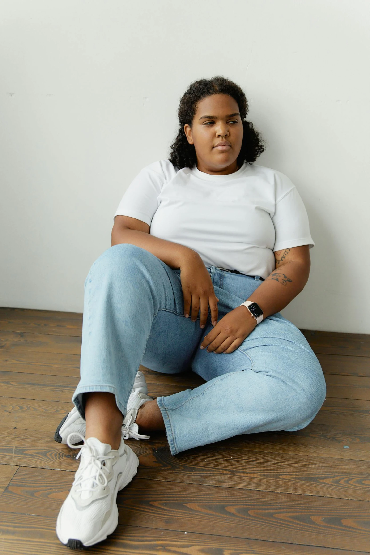 a woman sitting on the floor in jeans and white shoes