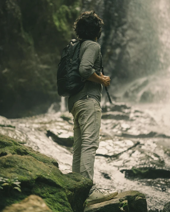 a woman with a backpack stands on a rock by a waterfall