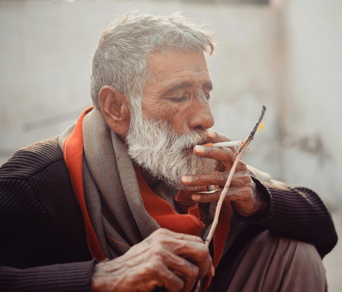 an older man with a white beard holding a cigarette and smoking