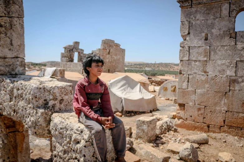 young man sitting in front of ruins of building