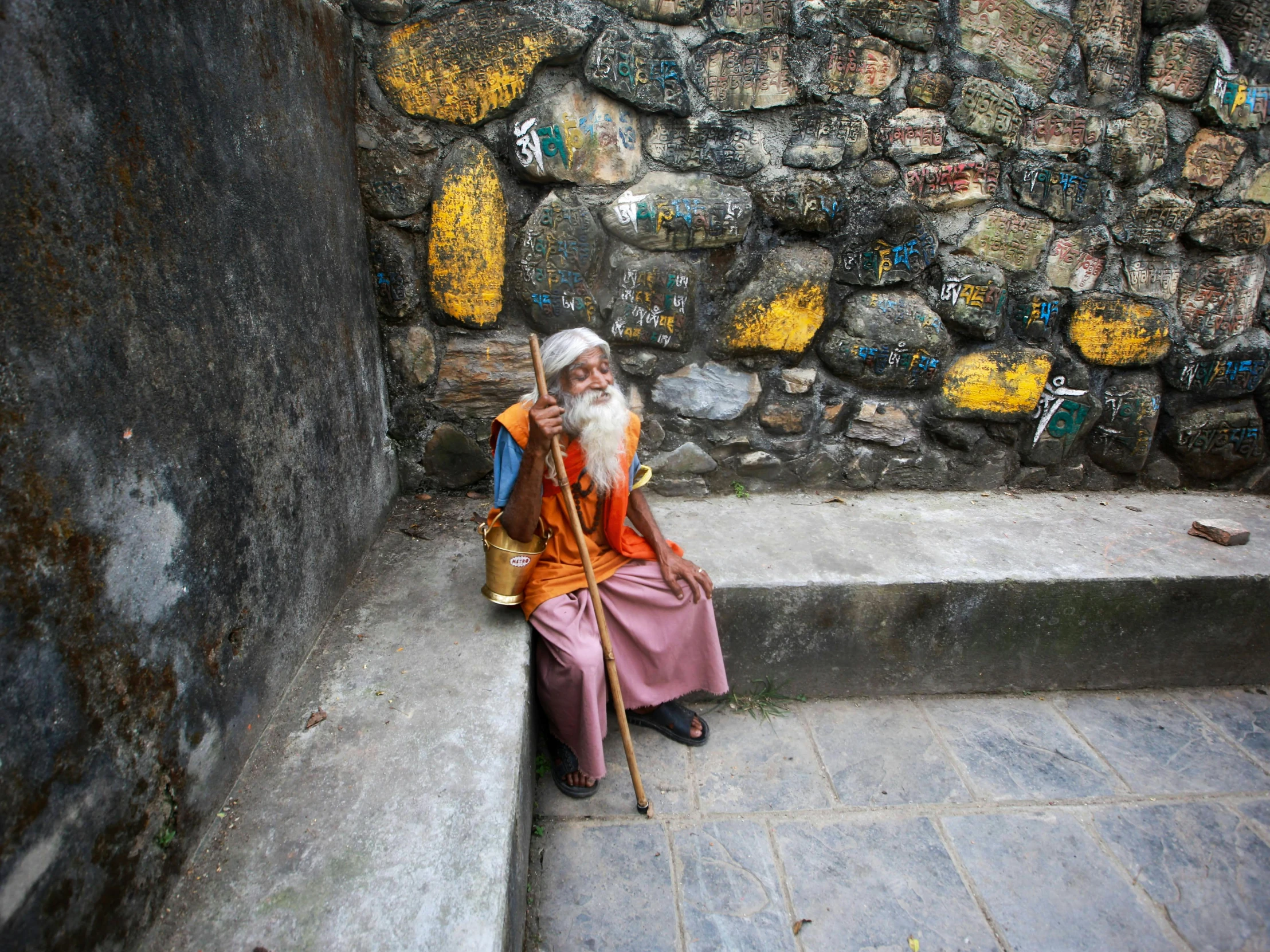 old man sitting on the steps outside near a stone wall