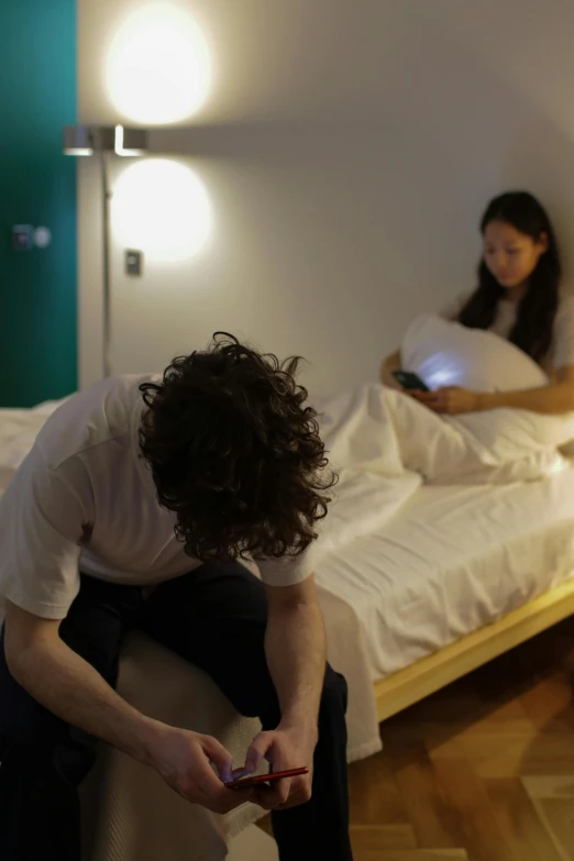 a person sits on the edge of a bed with a phone in hand