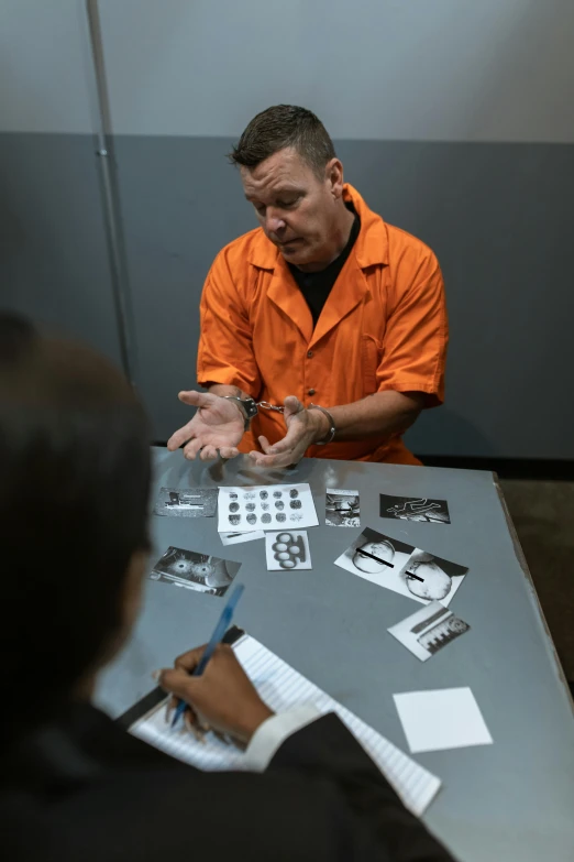 a man with an orange shirt writing on papers and holding a pen