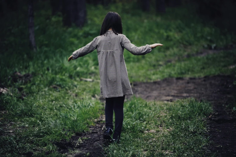 a small child in a striped dress stands on a grass covered path