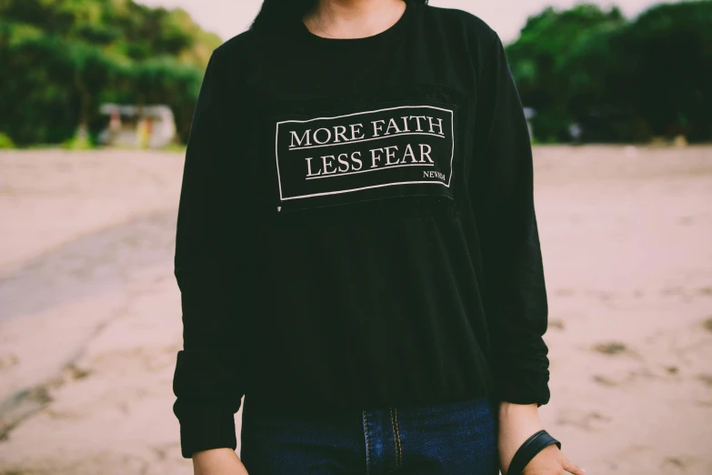woman standing on beach with sign that says more faith less fear