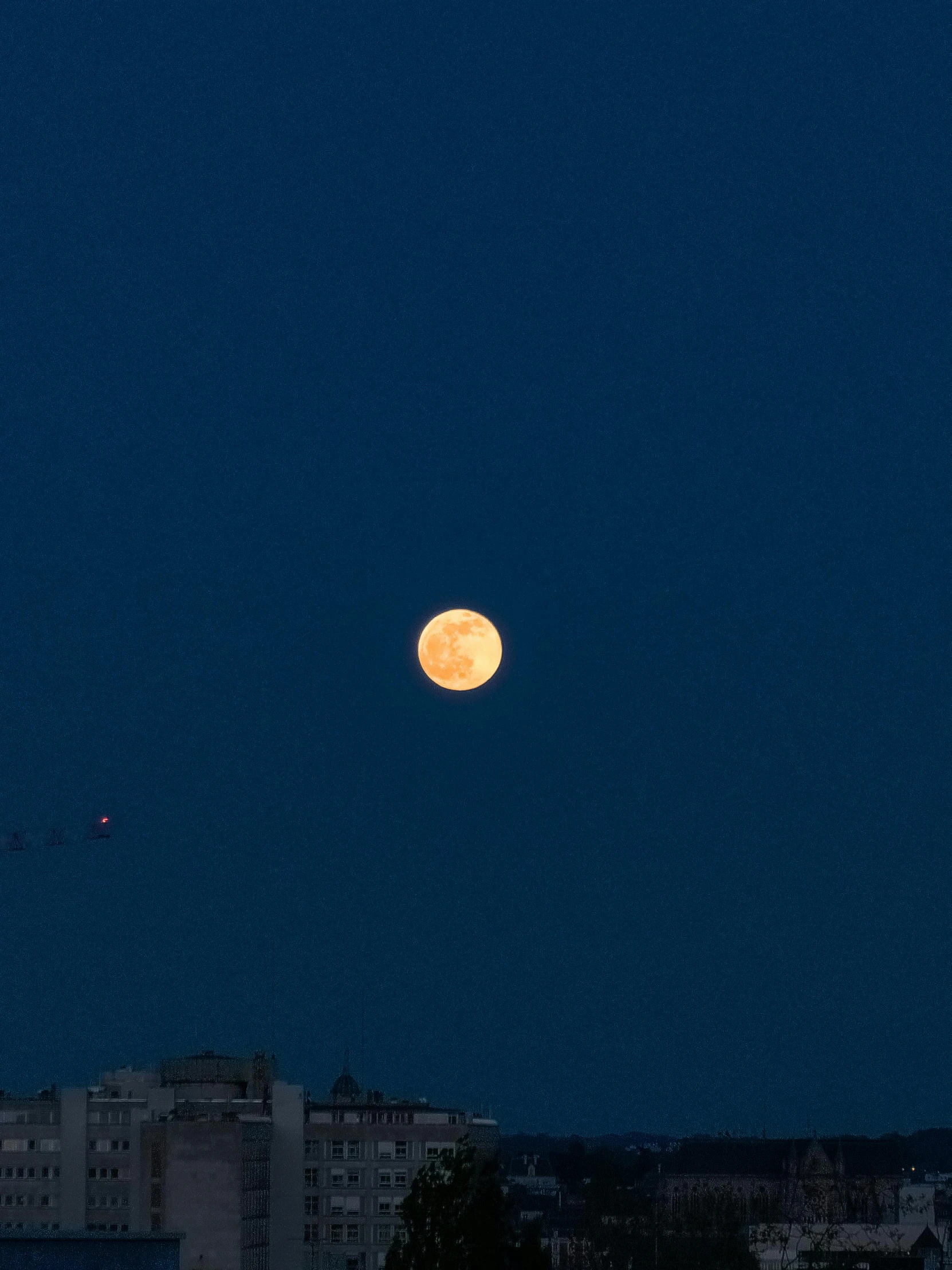 a full moon sitting in the sky over a city at night