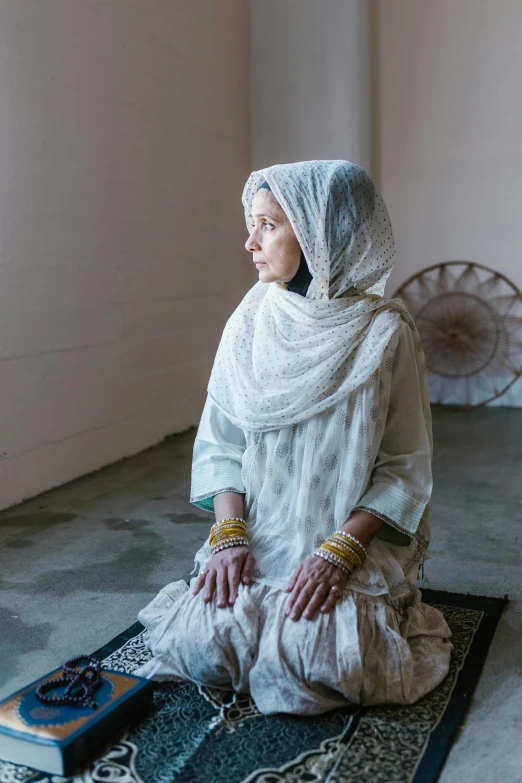 a woman wearing a white and gold dress sitting on a rug