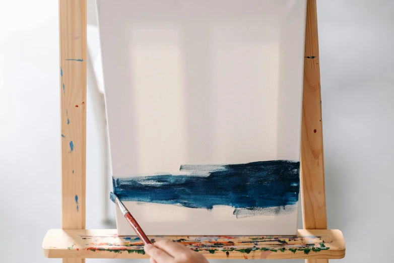 a person holds up a paintbrush and painting an easel with an abstract brush