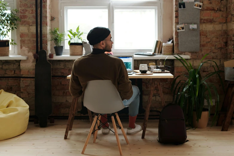 a man sits at his laptop in front of a brick wall