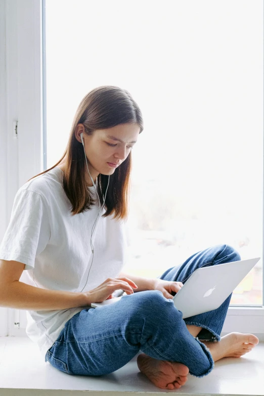 a girl sitting on the windowsill, looking down at soing while listening to her book