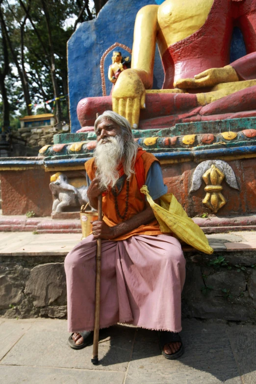 an elderly person sitting on the ground in front of a statue