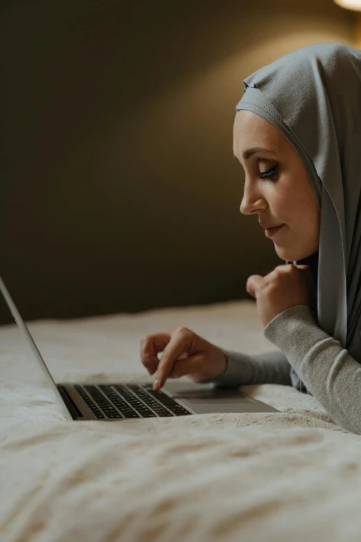 a young woman laying on her bed while using a laptop computer