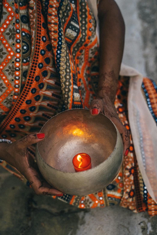 a close up of a person holding a bowl with a lit candle in it
