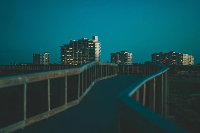 a long, empty bridge stretches over a body of water into the dark city