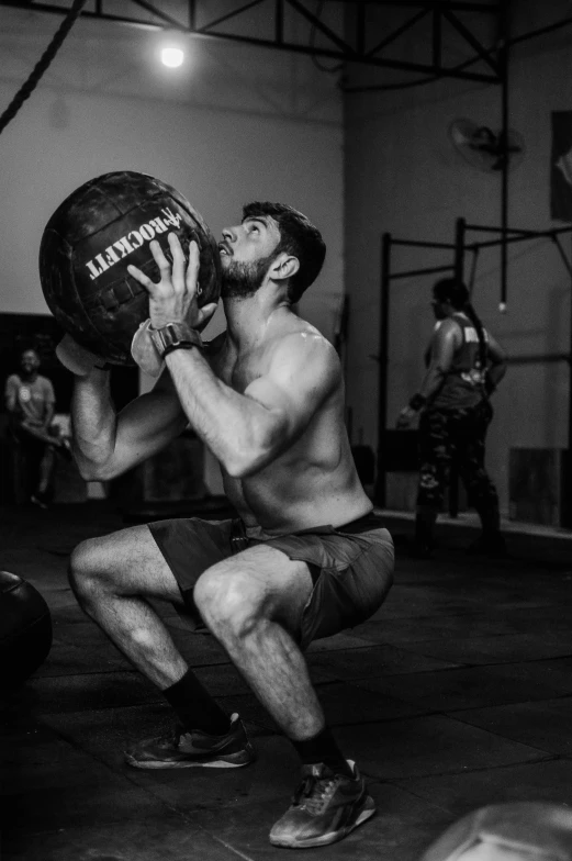 a shirtless man squatting down on the floor with a ball in his hands