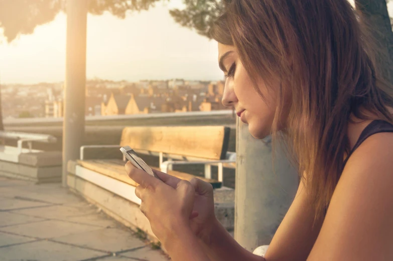 a girl sits on a bench while looking at her cell phone