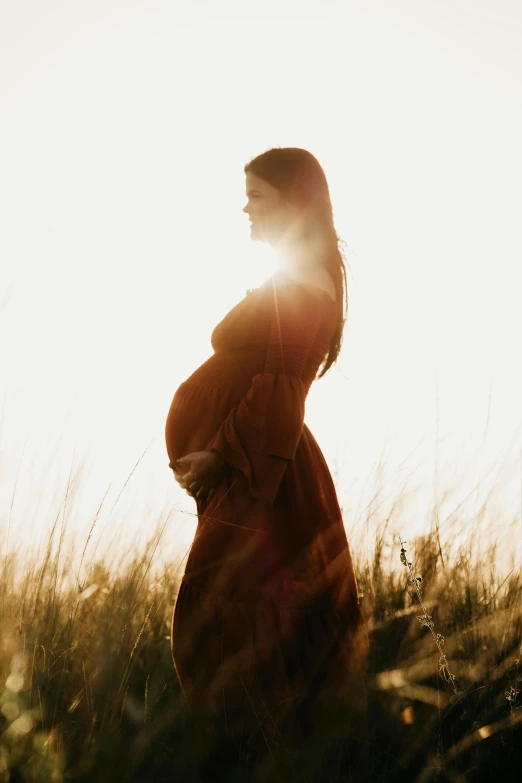 a woman stands in an open field at sunset