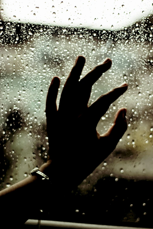 a hand reaching out of a window that is covered in rain drops