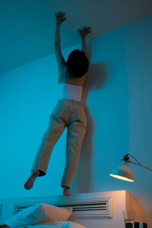 a boy jumping up from a bed with a blue light on