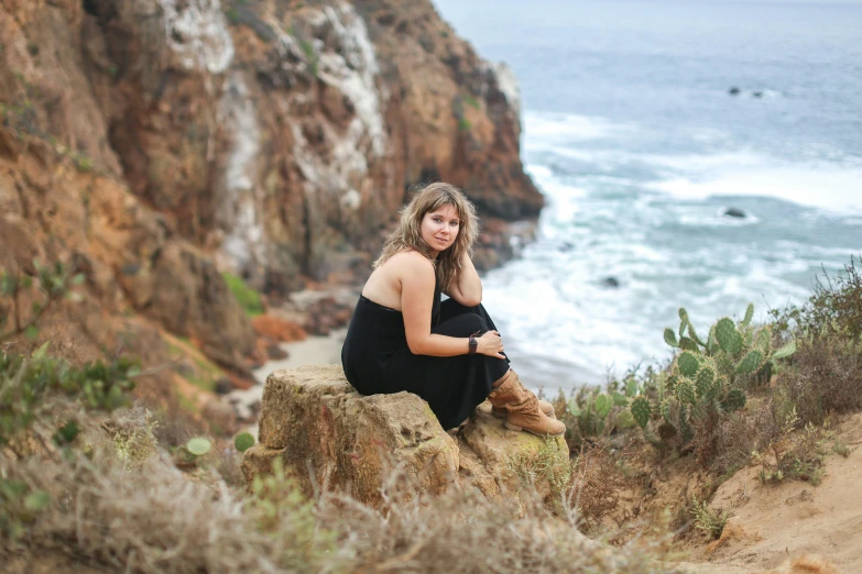 a woman sitting on a rock overlooking the ocean