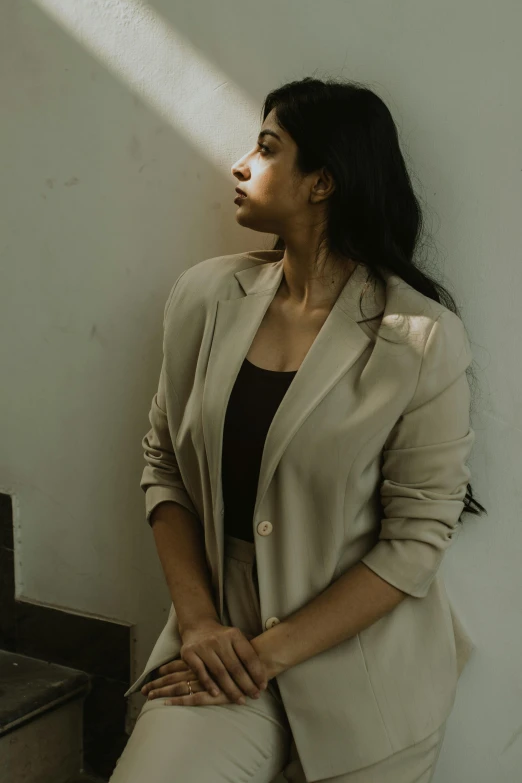 a woman wearing a tan blazer and pants leaning against a wall