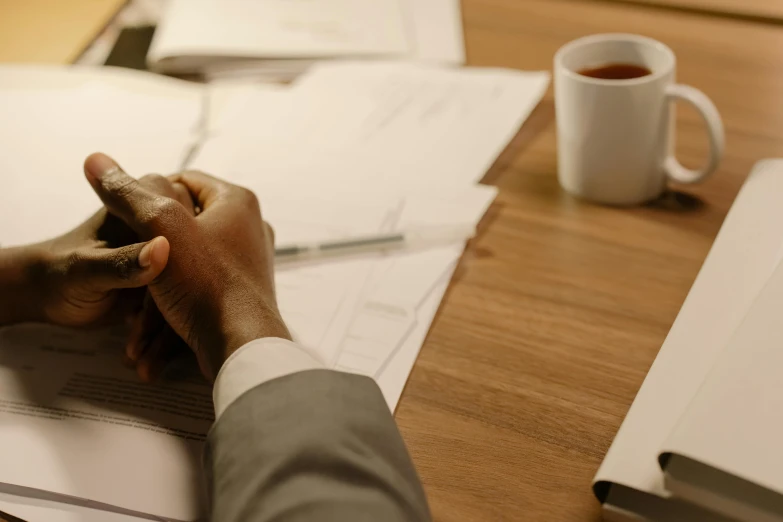 a person holding their hand out to one another with papers next to a coffee mug