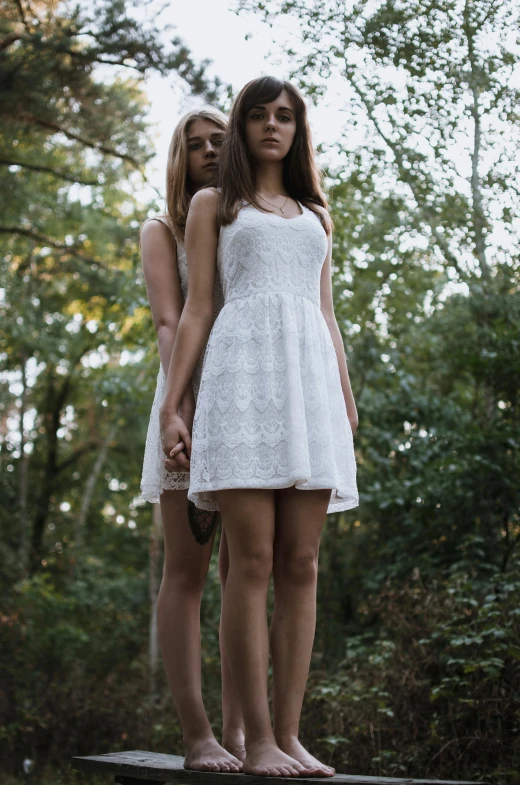 two women in white outfits standing on a wooden ledge