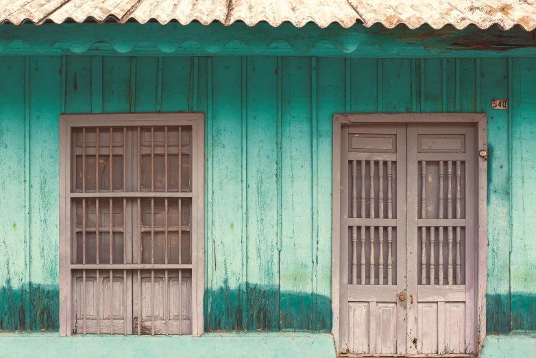 a green building with wooden windows with bars on it