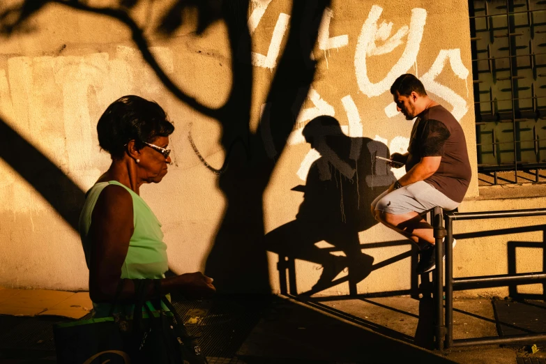 man sitting in the shade talking on the phone while woman passes him by on a stair case