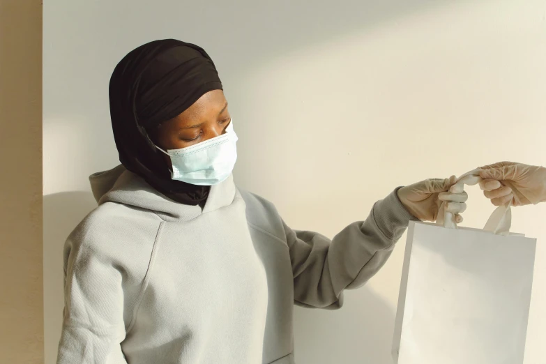 a woman wears a face mask and gloves while holding a small bag