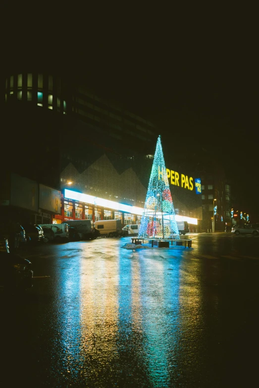 lit christmas tree in the middle of a rainy city at night