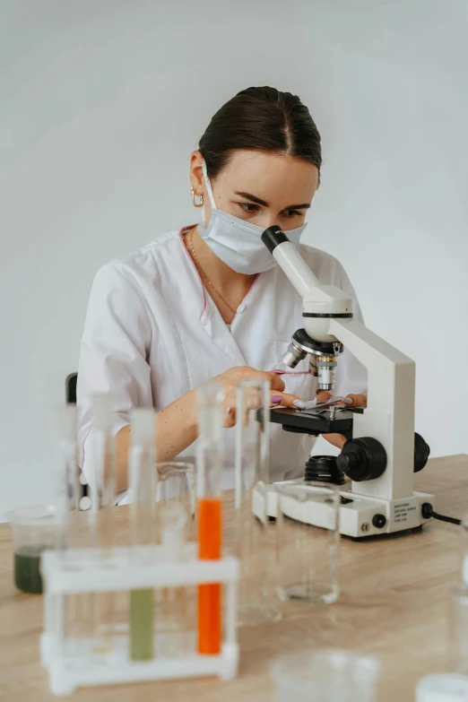a woman with a white mask sits at a table in front of a microscope