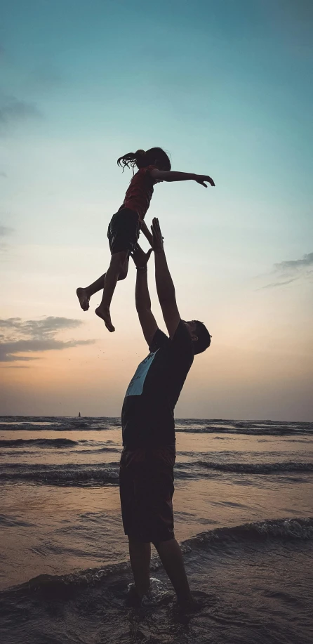 a man and little girl on the beach in front of a colorful sky