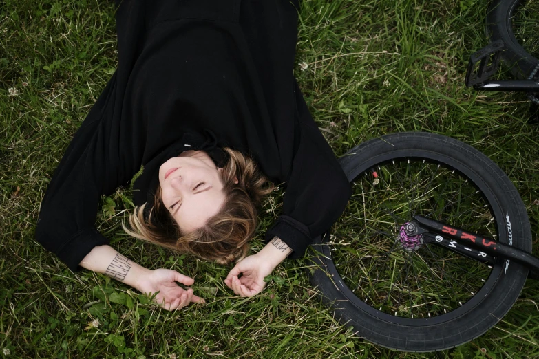 woman in black shirt and black pants laying on grass near bike tire