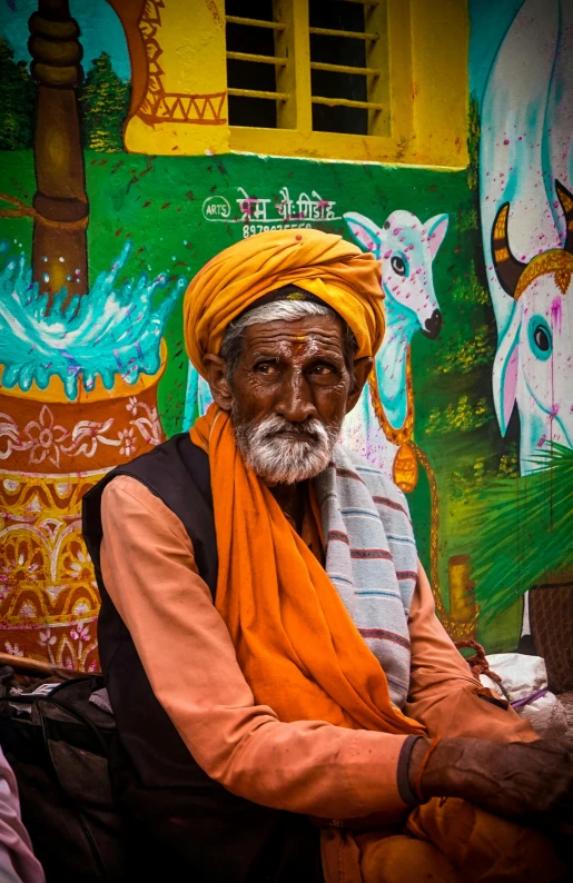 a man with a turban sits in front of a colorful wall