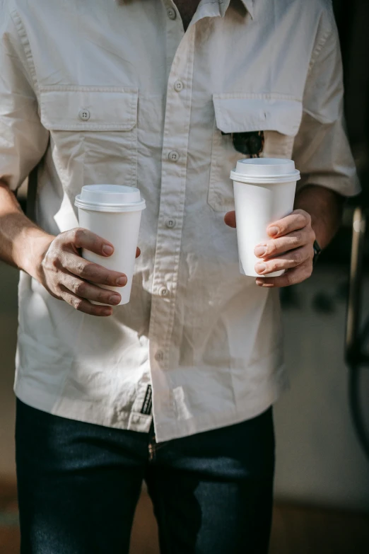 a man is holding two coffee cups in both hands