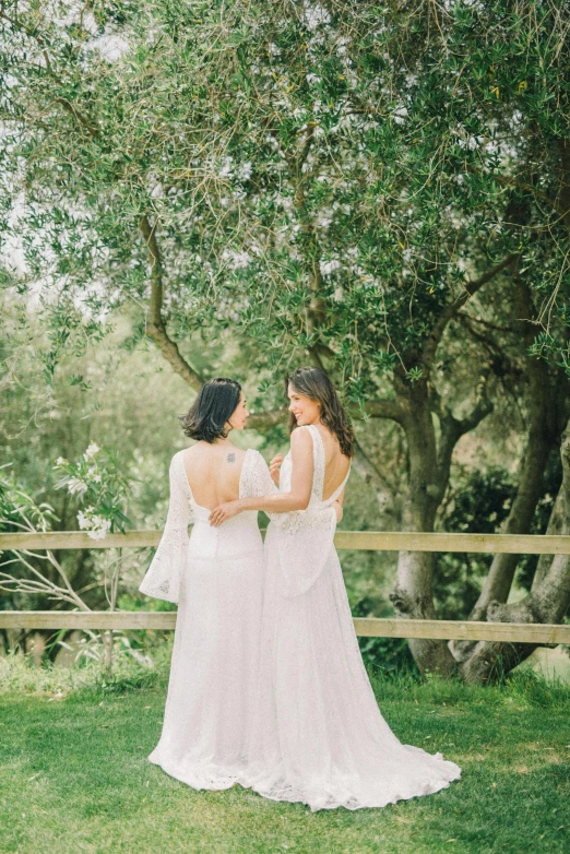 two women in dresses standing next to each other near trees