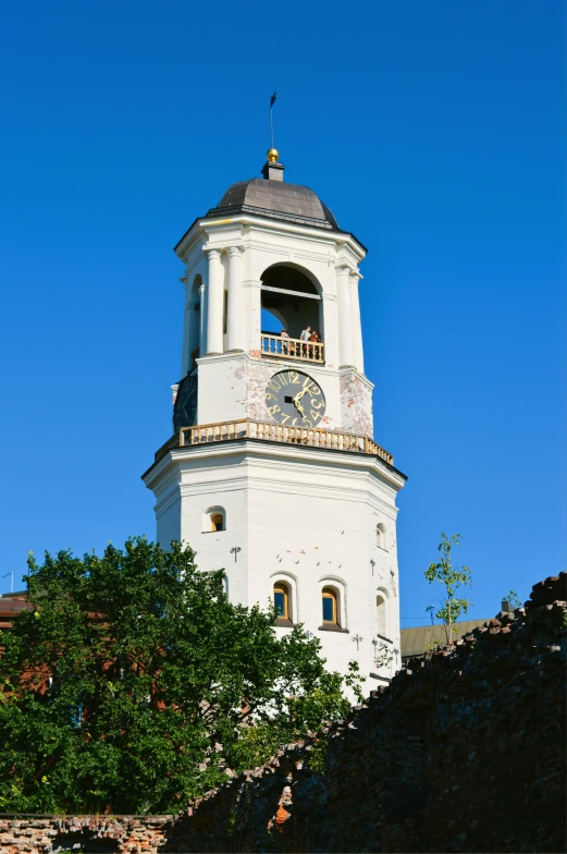 a white clock tower against a blue sky with trees below