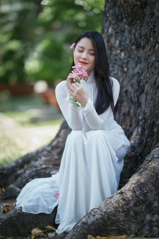 a woman sitting in the shade of a tree with flowers