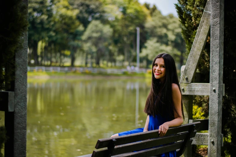 a woman in a dress sitting on a bench next to a lake