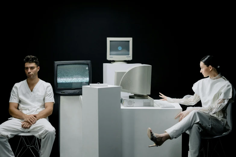 two people sitting on pedestals facing one another with an old television in the background