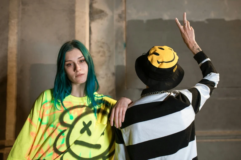 two people, one with green hair and another in  shirts are wearing a smiley face on the wall