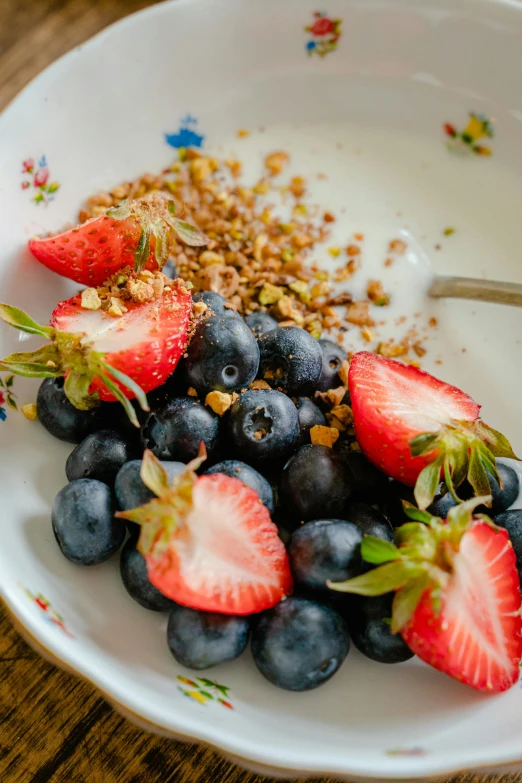 a plate of cereal, fruit and yogurt with strawberries and blueberries