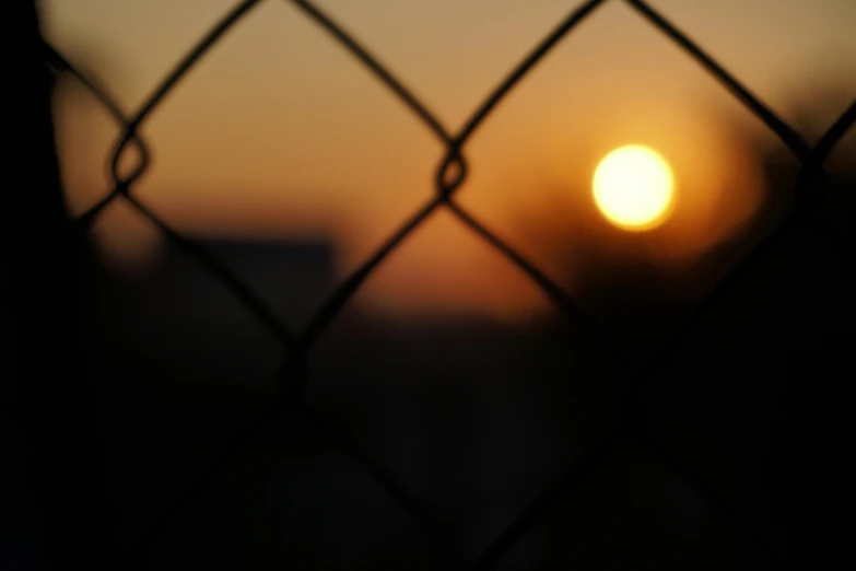 the sun is setting behind a fence