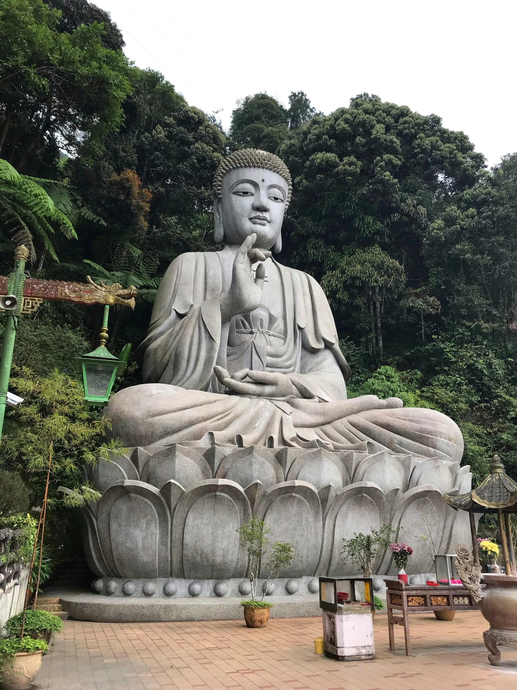 a stone buddha sitting outside with a green mountain behind it