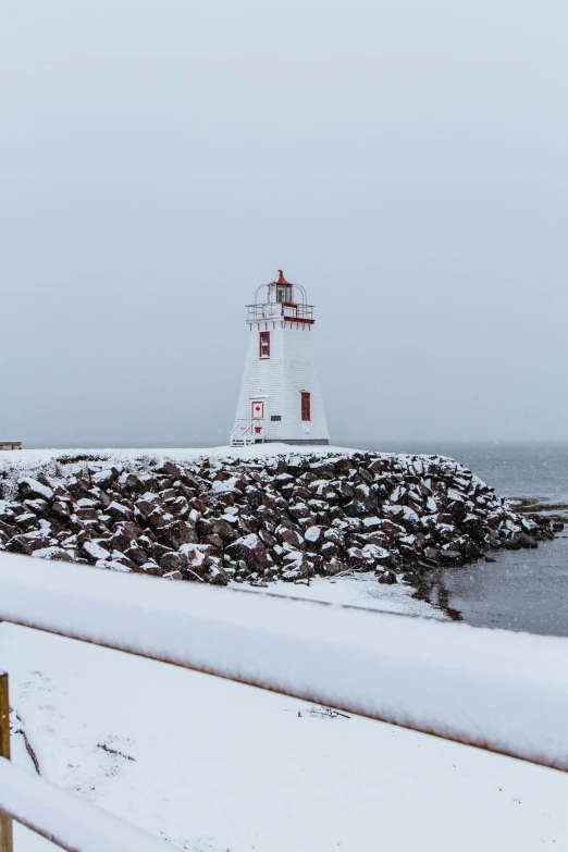 a lighthouse on the coast in wintertime with snow