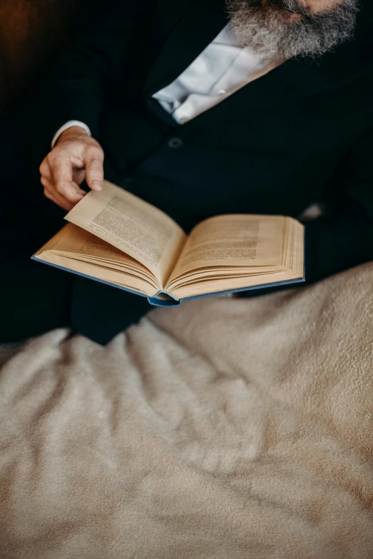 a man in a suit sitting in bed while holding an open book