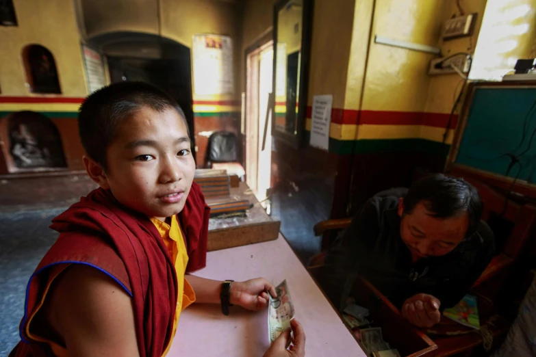 a boy in a buddhist robe sits at a table