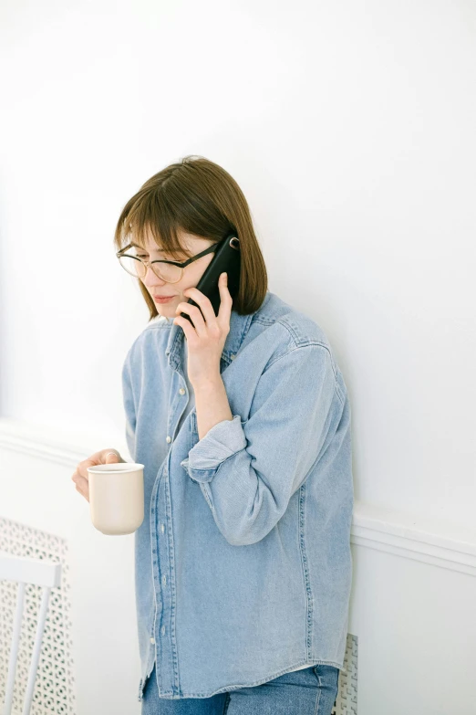 woman wearing glasses talking on a cell phone and holding a cup