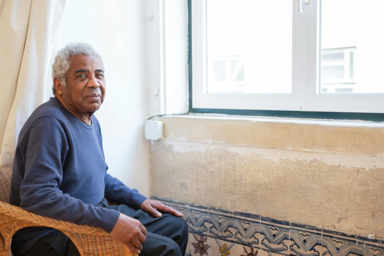 an elderly man in blue shirt sitting next to window